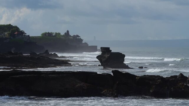 Grassy Headland Overlooking Temple On Coastline, Rolling Waves And Steep Cliffs, Misty Horizon And Vibrant Green Pasture, Cultural Landmark With Sacred Atmosphere, Tanah Lot temple, Bali, Indonesia