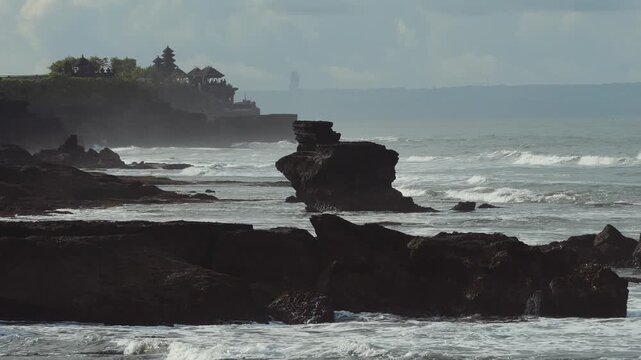 Coastal Bali Temple Silhouette Above Ocean, Misty Horizon With Layered Cliffs And Lush Green Foreground, Traditional Meru Shrine Roofs Rising From Rock Outcrop, Tranquil Sunset Tones And Spiritual