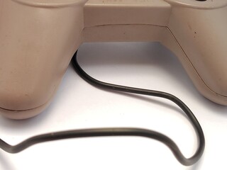 Close-up view of a black cable extending from the dirty, worn back of a retro gaming controller, isolated on a white background © Ricko Destu