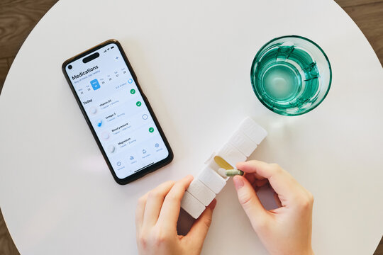 Female hands preparing daily pills from an organizer with medication tracking app on phone
