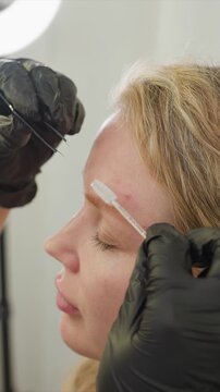 Close up shows person undergoing professional eyebrow grooming focusing on precise application of thread to remove hair. setting includes soft studio lights and neutral background
