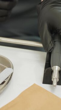 Close up view of gloved hand using electric nail drill on another person foot with pedicure tools like files and buffers visible. scene is set in professional beauty treatment environment