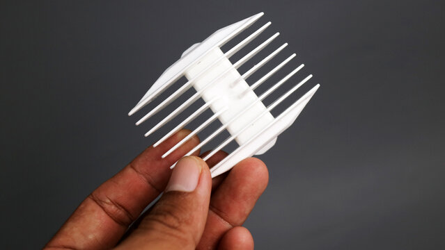 Hand holding a white plastic hair clipper comb attachment against a dark