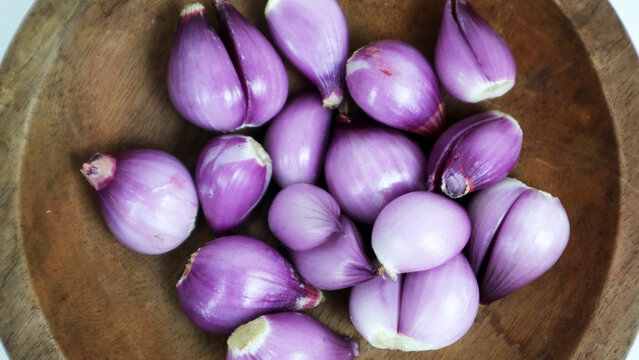 Top view of peeled fresh red shallots placed inside a traditional wooden bowl