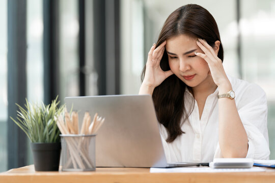 Stressed Asian Businesswoman Holding Head in Hands in Front of Laptop