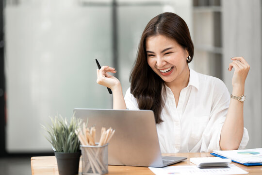 Joyful Asian Businesswoman Laughing while Working on Laptop at Office Desk