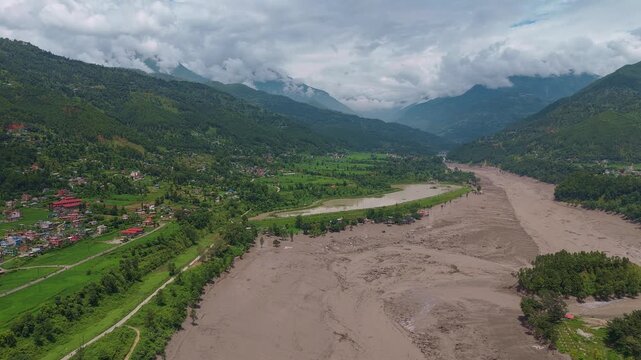 Aerial view of a row of buildings surrounded by flood mud beside a canal after a flash flood in a Nepal river valley