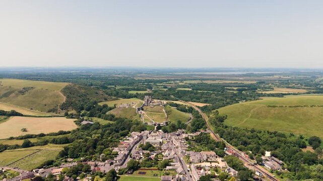 Corfe Isle of Purbeck Dorset, England, forward drone footage over Corfe village with Corfe Castle dominating the countryside on sunny Summer day with extensive views to misty horizon