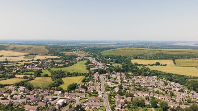 Corfe Isle of Purbeck Dorset, England, high,slow,forward drone footage Corfe village with Corfe Castle beyond on sunny Summer day with views across to Poole harbour and misty horizon