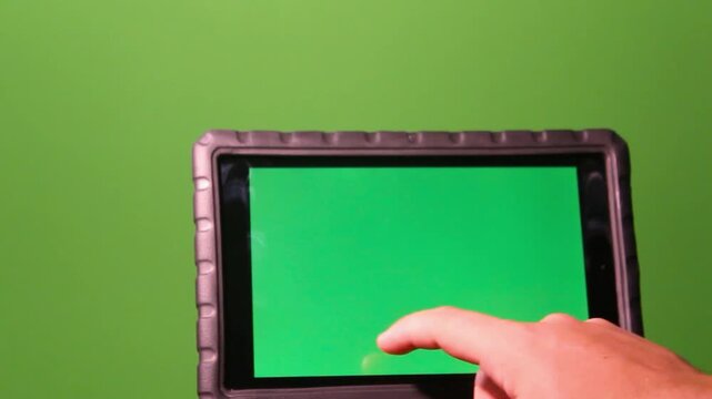 Hand touching digital tablet screen against a green background