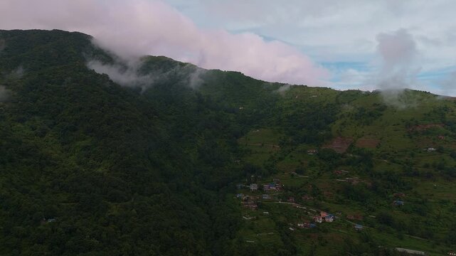 Aerial view of a cloud-capped forested mountain with terraced village settlements climbing the slopes in the hills of Nepal