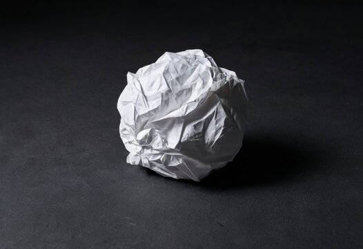 Crinkled white paper ball on dark background, minimalist texture shot