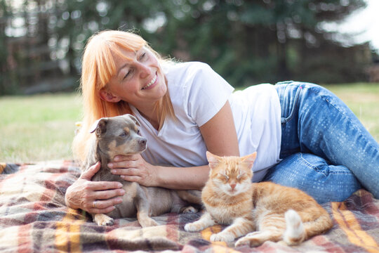 Happy Blonde Woman Relaxing with Small Fluffy Dog on Outdoor Picnic Blanket