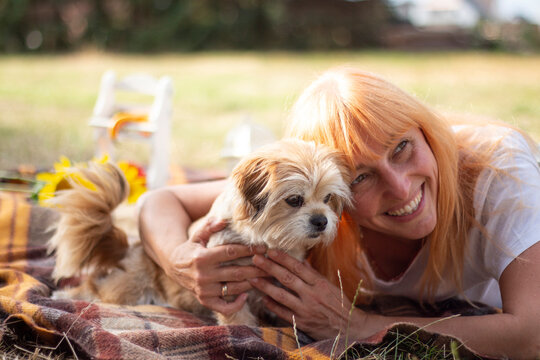Happy Woman Lying on Picnic Blanket and Cuddling Her Orange Cat Outdoors