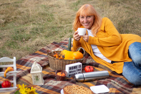 Smiling Blonde Woman Enjoying Cozy Autumn Picnic with Food and Warm Drink Outdoors