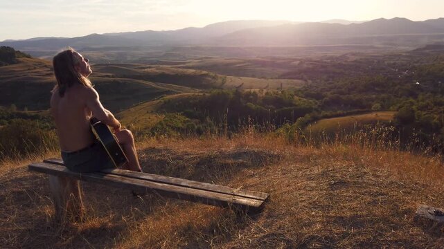 Slow motion view of silhouette of shirtless guitar player with mountain view during sunset horizon 