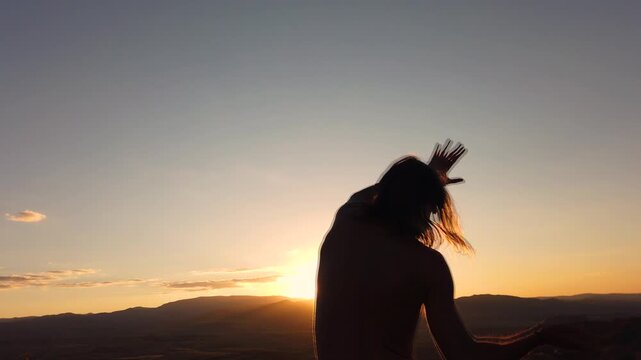 Slow motion rear view of shirtless man with long hair dancing at sunset on a mountain ridge