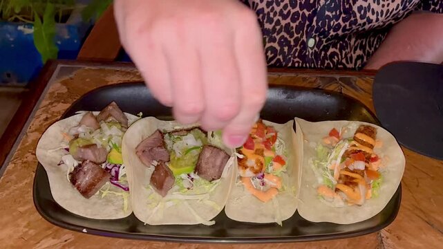 Close up of the man's hand squeezing the lime on top of tacos in Mexican restaurant