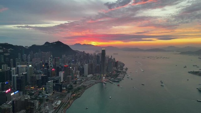 Red sky over Victoria Peak and the Hong Kong Island waterfront, continuing slow drone pan as neon begins to glow on the dense towers of Wan Chai and Central at dusk