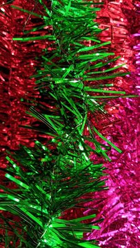 Colorful Christmas tinsel with green, pink and red metallic strands creating a vibrant vertical festive background for holiday designs.