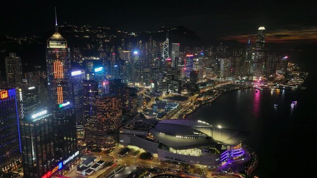 Aerial glide over the neon lit towers of Wan Chai at night, tower, the convention centre and the curving harbourfront of Hong Kong Island glowing far below