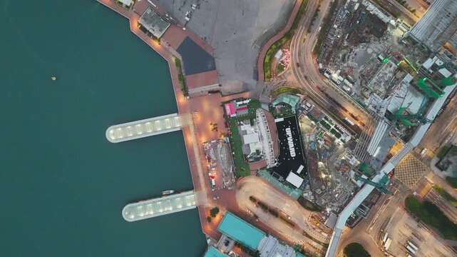 Top down drone view of the Central ferry piers and harbourfront in Hong Kong at dawn, the observation wheel, piers and teal Victoria Harbour water in a graphic pattern