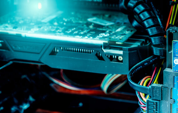 Computer graphics card and SATA cables inside a desktop case, exposed circuit boards, heatsink fins and bundled power wiring beside a storage drive, with visible dust on connectors and hardware.