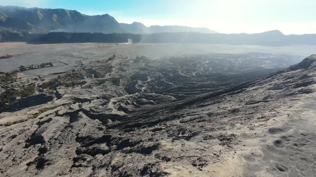 POV walking along the edge of Mount Bromo, revealing a vast Indonesian volcanic landscape with rugged terrain, surrounding mountains, and expansive natural scenery