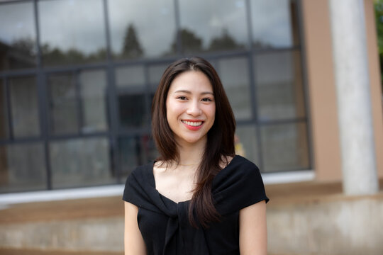 Smiling Asian woman in black blouse portrait outdoors near modern building