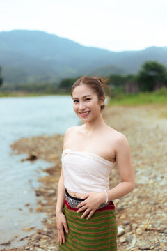 Young Asian woman smiling beside mountain lake in traditional patterned skirt