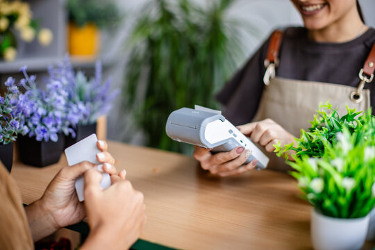 In a vibrant flower shop, a customer hands over a payment card while the florist smiles and holds a card reader.