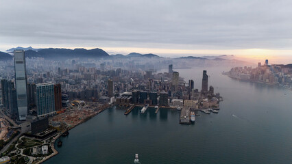Fototapeta premium Aerial drone panorama of Hong Kong at sunrise, looking along Victoria Harbour past Tsim Sha Tsui to Hong Kong Island with fog on the hills and a glowing horizon