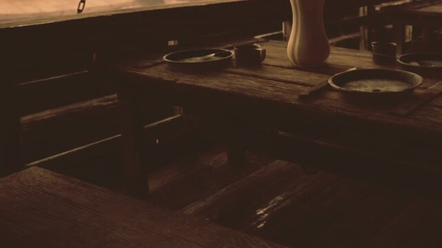 In a cozy, rustic setting, a wooden table displays simple tableware, including plates and a jug. The warm light adds a touch of comfort, creating an inviting atmosphere for shared meals.
