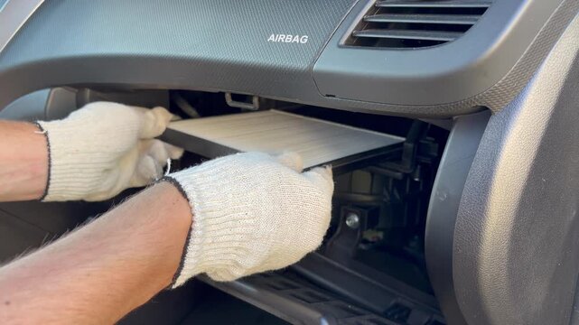 A mechanic installs a new cabin air filter into the car's dashboard. Automotive maintenance, vehicle repair, HVAC system servicing, and DIY car care