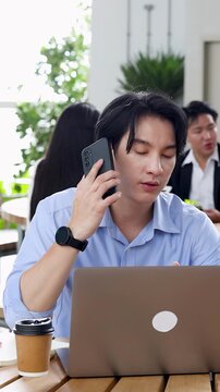 Asian Businessman Answering Smartphone While Working on Laptop in Cafe
