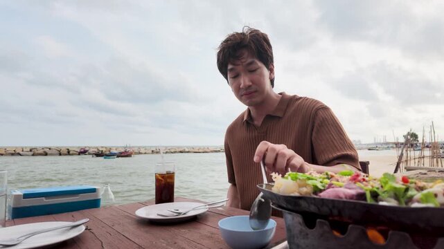 Asian Man Eating Seafood Soup at Outdoor Beachside Restaurant