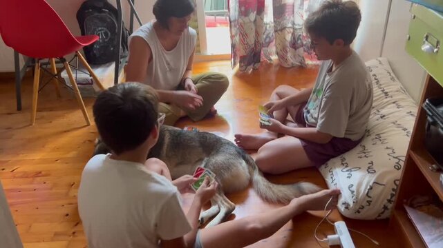 A mother and her two sons play a card game on the floor with their dog in Kalamata, Greece