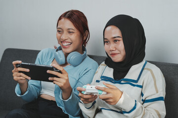 Two excited young Asian women are using handheld console device and joystick to play game together. © ChristyMerry
