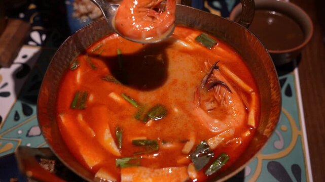 Close-up of authentic Thai Tom Yum Goong soup with shrimp, lemongrass, lime leaves, and chili, served in metal bowl, symbol of Thailands famous spicy and sour cuisine and Asian street food culture.