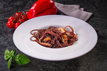 Black squid ink pasta with octopus and mussels on white plate with cherry tomatoes and basil © Andrei Starostin