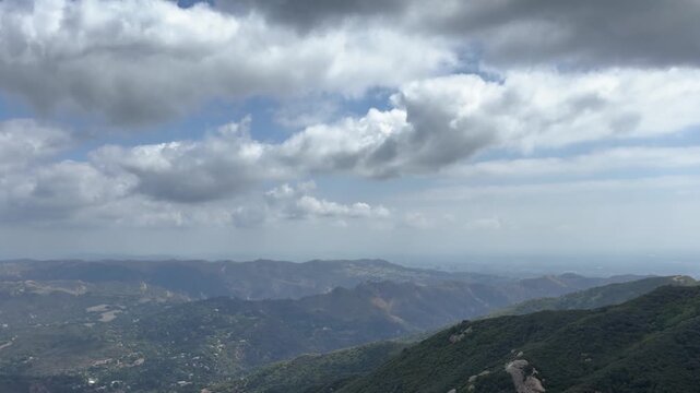 Time lapse of white cumulus clouds drifting across a blue sky over the forested ridges and canyons of the Santa Monica Mountains, seen from Lois Ewen Overlook in Topanga, California.