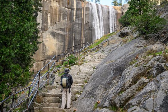Hiker standing on steep granite steps and admiring the Vernal Fall. Yosemite National Park. California. USA.