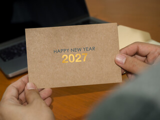 Person holding recycle kraft paper Happy New Year 2027 greeting card at a desk. Sustainable stationery, eco-conscious communication, corporate greetings and responsible business concepts. © tete_escape