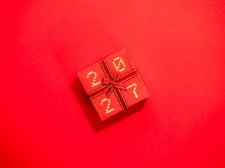 Red gift box with digital-style 2027 numbers and decorative ribbon on a vivid red background, ideal for new year celebrations, holiday promotions, festive greetings and seasonal marketing concepts. © tete_escape