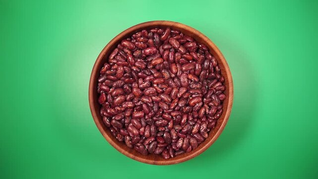 Red beans rotating in a wooden bowl on the green table, top view, close-up