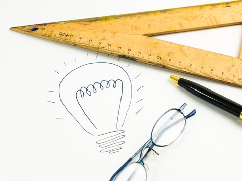 Drawn lightbulb, set square, reading glasses and ballpen on white paper