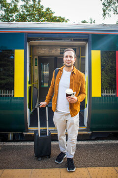 Male passenger with suitcase awaits a train on a London platform