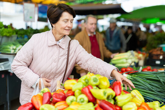 Casual senior female customer choosing organic vegetables while walking at local market