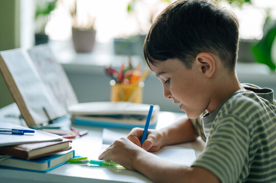 A young boy writes his homework at a desk indoors