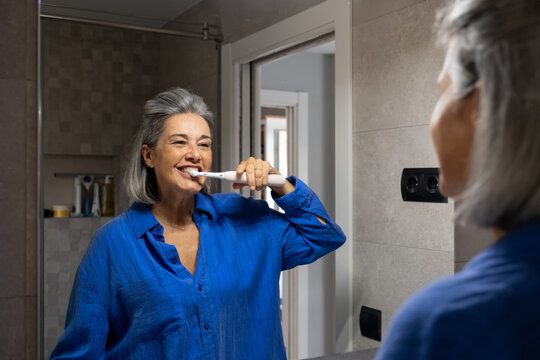 Mature woman brushes teeth in the bathroom mirror